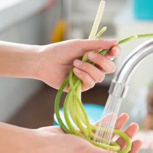 Close view of hands washing green onions under sink faucet.