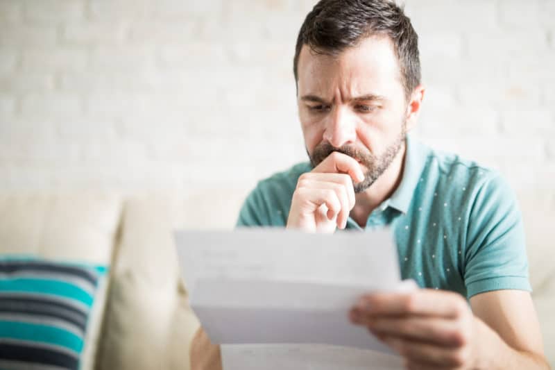 Man sweating and reading an energy bills with concerned look on his face.